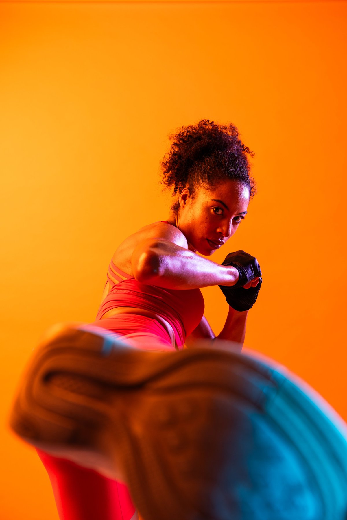 Sportive black hispanic woman wearing sportswear training in fitness studio, colorful dramatic lighting - African-american female athlete doing sport workout