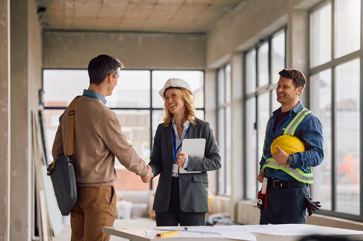 Happy project manager and construction worker greeting a building contractor during a meeting.