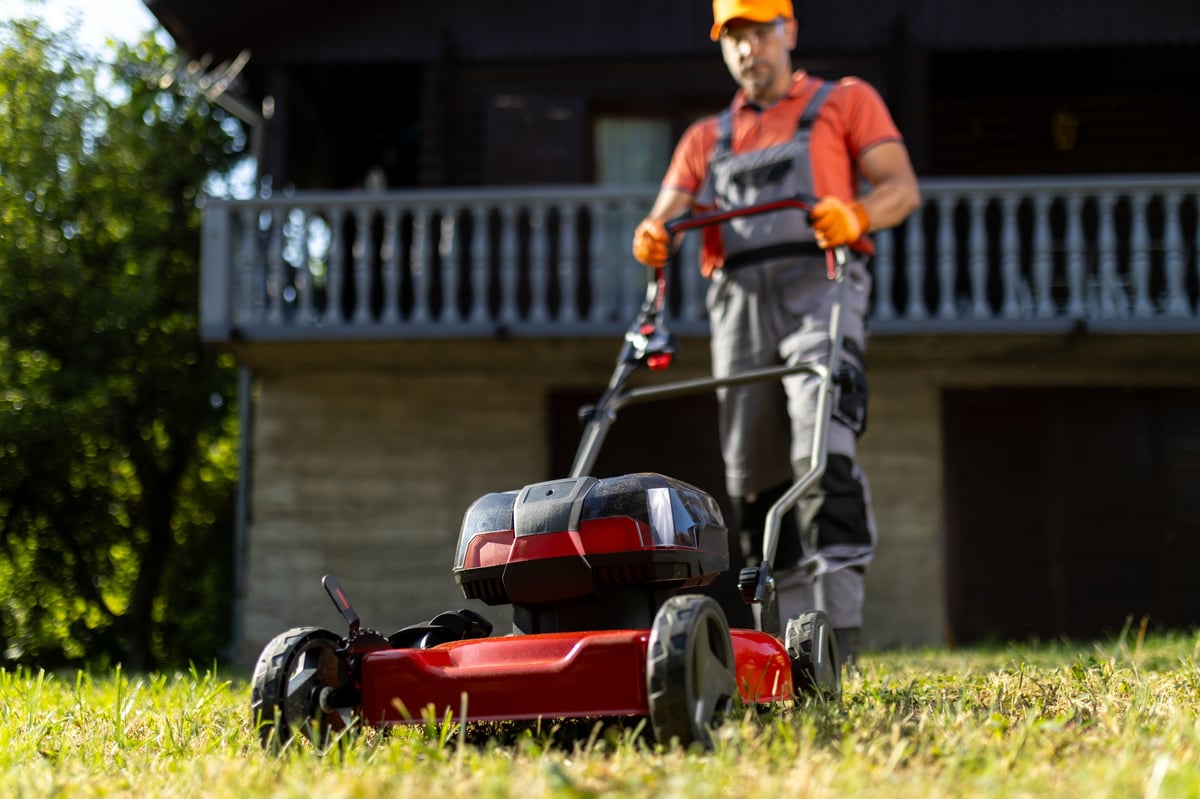 A man pushes a cordless lawn mower across a residential lawn while performing home garden maintenance