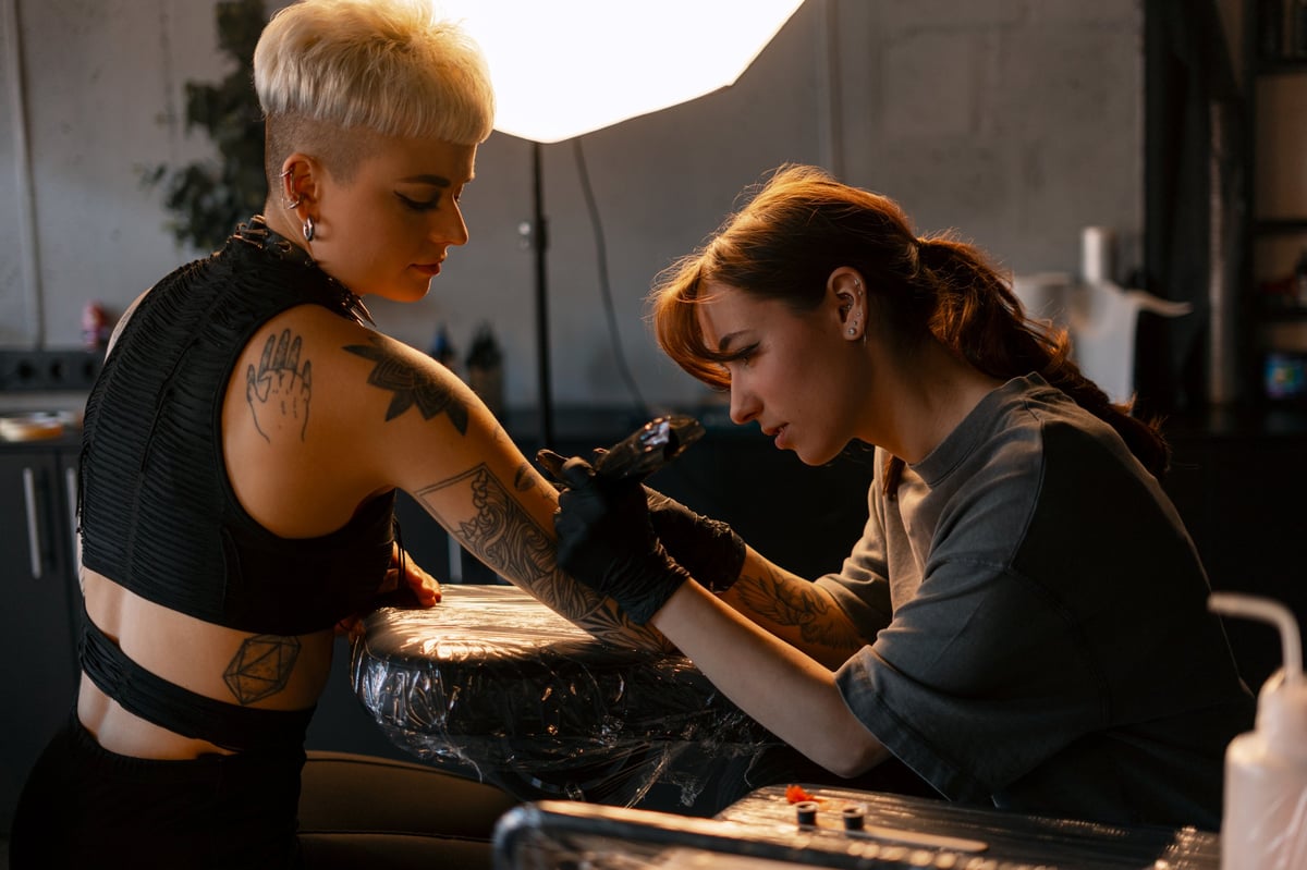 Professional tattoo artist wearing gloves skillfully applying ink on a young adult woman's arm in a clean studio