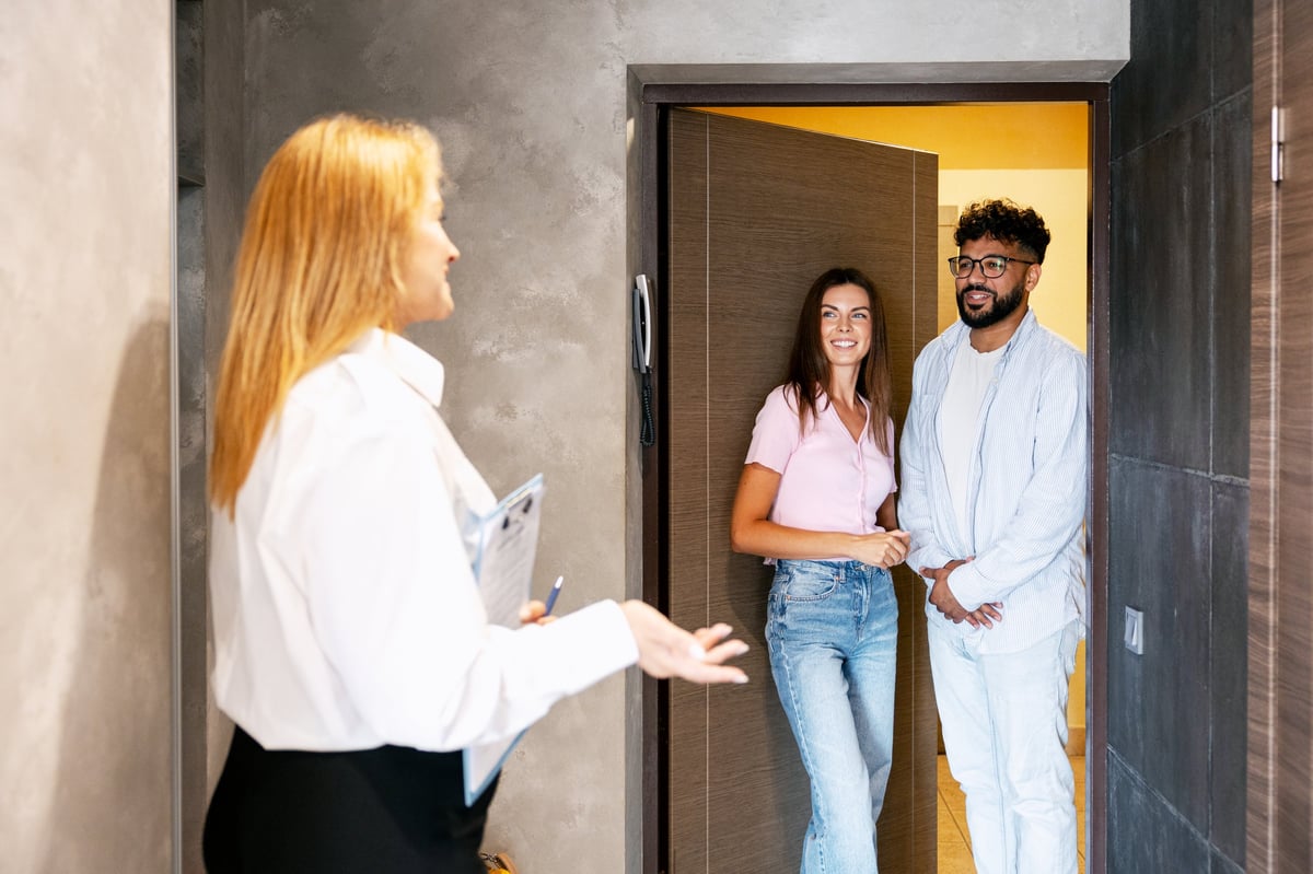 Real estate agent greeting a happy young couple at the apartment entrance for a property viewing, discussing key features
